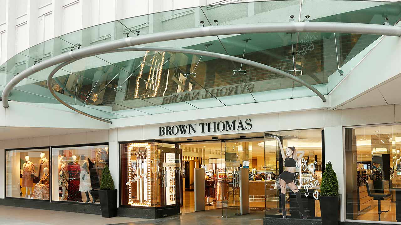 The image shows the entrance of a Brown Thomas store with large glass doors and fashion displays in the windows.